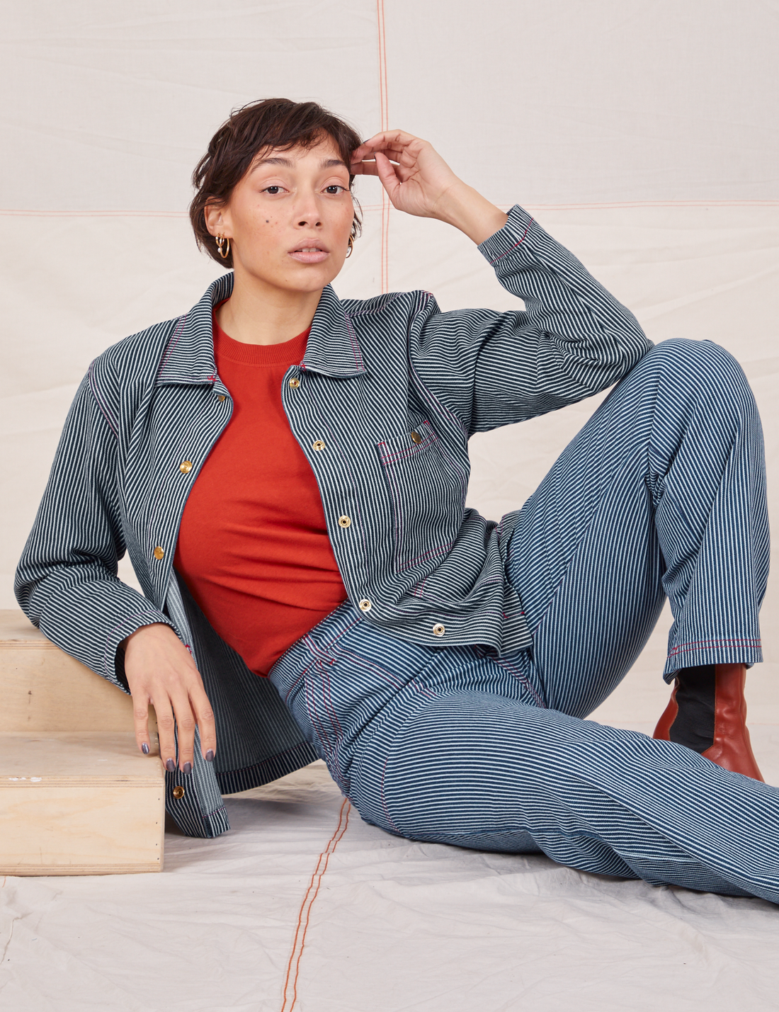 Tiara is sitting on the floor wearing Railroad Stripe Denim Work Jacket and matching Work Pants