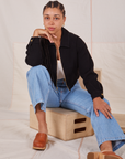 Gabi is sitting on a wooden crate wearing Ricky Jacket in Basic Black