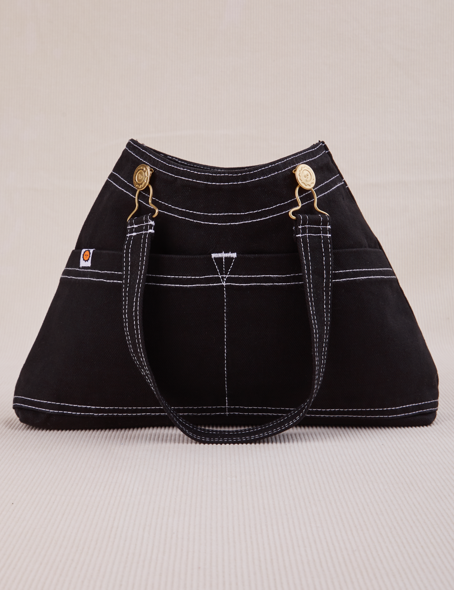 Overall Handbag in Black with handle strap hanging down front of bag.