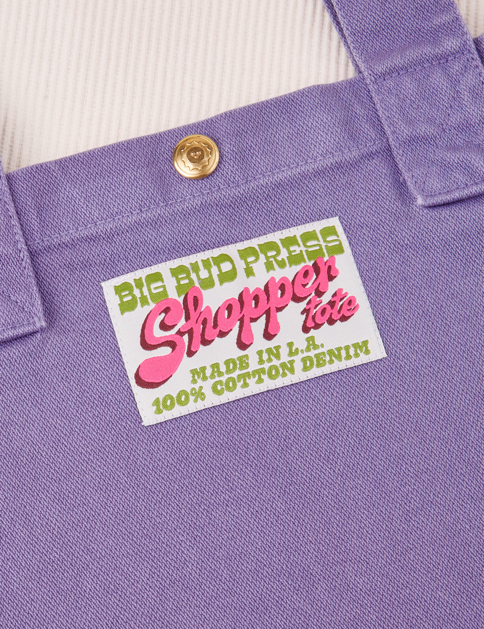 Sun Baby brass snap on Shopper Tote Bag in Faded Grape. Bag label in green and pink text that reads &quot;Big Bud Press Shopper Tote, Made in L.A., 100% Cotton Denim&quot; on a white background