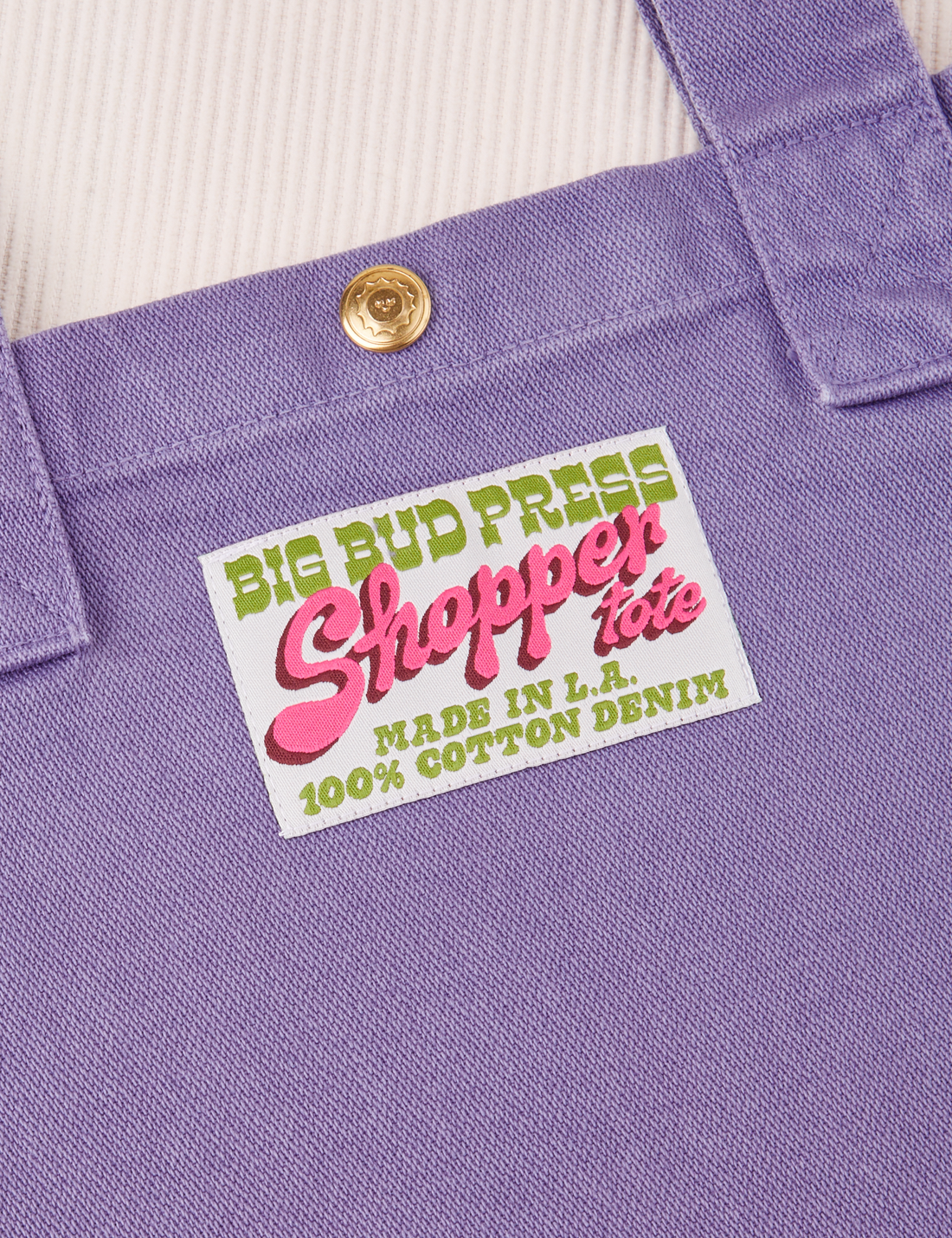 Sun Baby brass snap on Shopper Tote Bag in Faded Grape. Bag label in green and pink text that reads "Big Bud Press Shopper Tote, Made in L.A., 100% Cotton Denim" on a white background