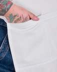 Close up of Sam's hand in the pocket of a Full Denim Apron in Stone White