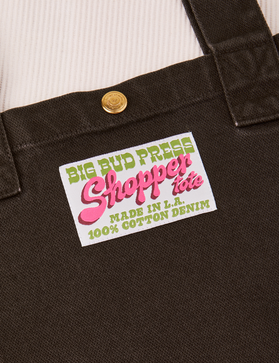 Sun Baby brass snap on Shopper Tote Bag in Espresso Brown. Bag label with green and pink text that reads "Big Bud Press Shopper Tote, Made in L.A.,100% Cotton Denim" on white background