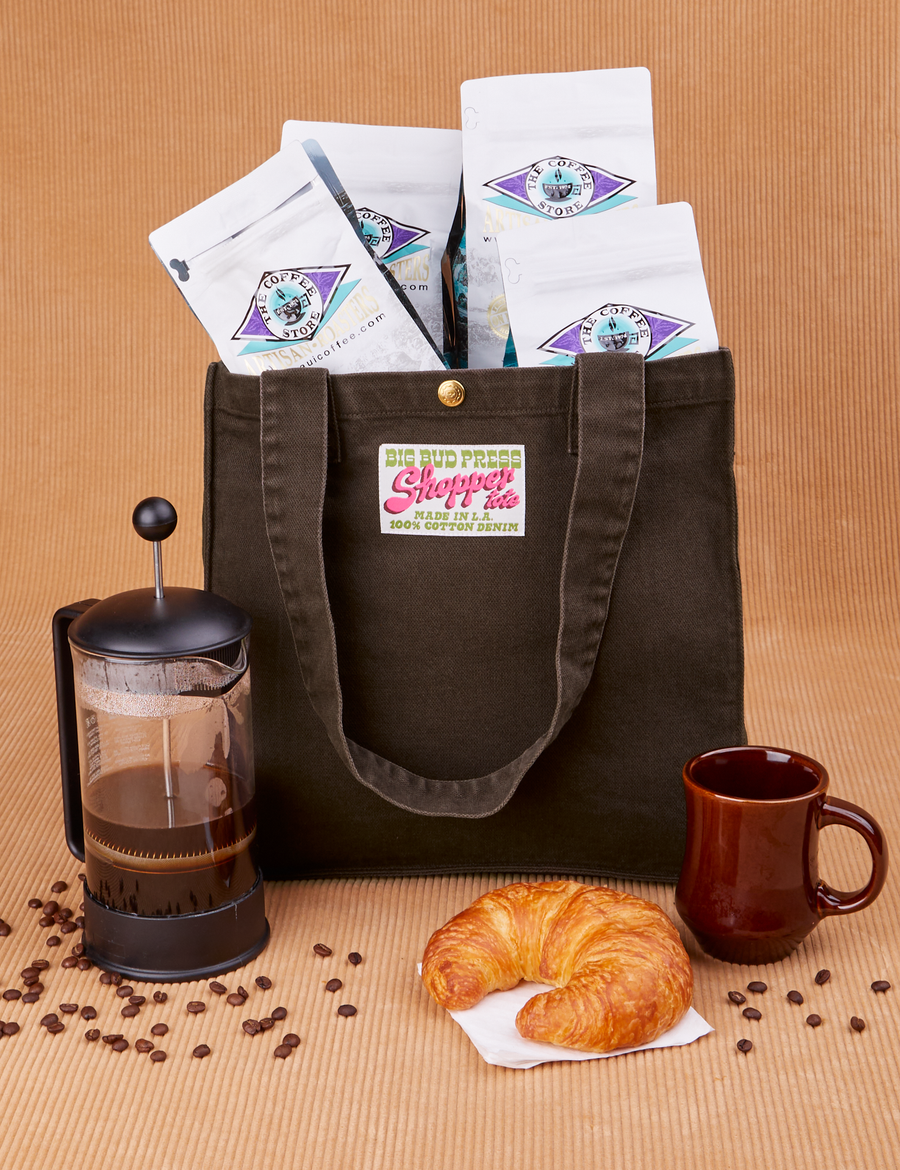 Shopper Tote Bag in Espresso Brown with bags of coffee inside. French Press, mug and croissant placed in front of bag.