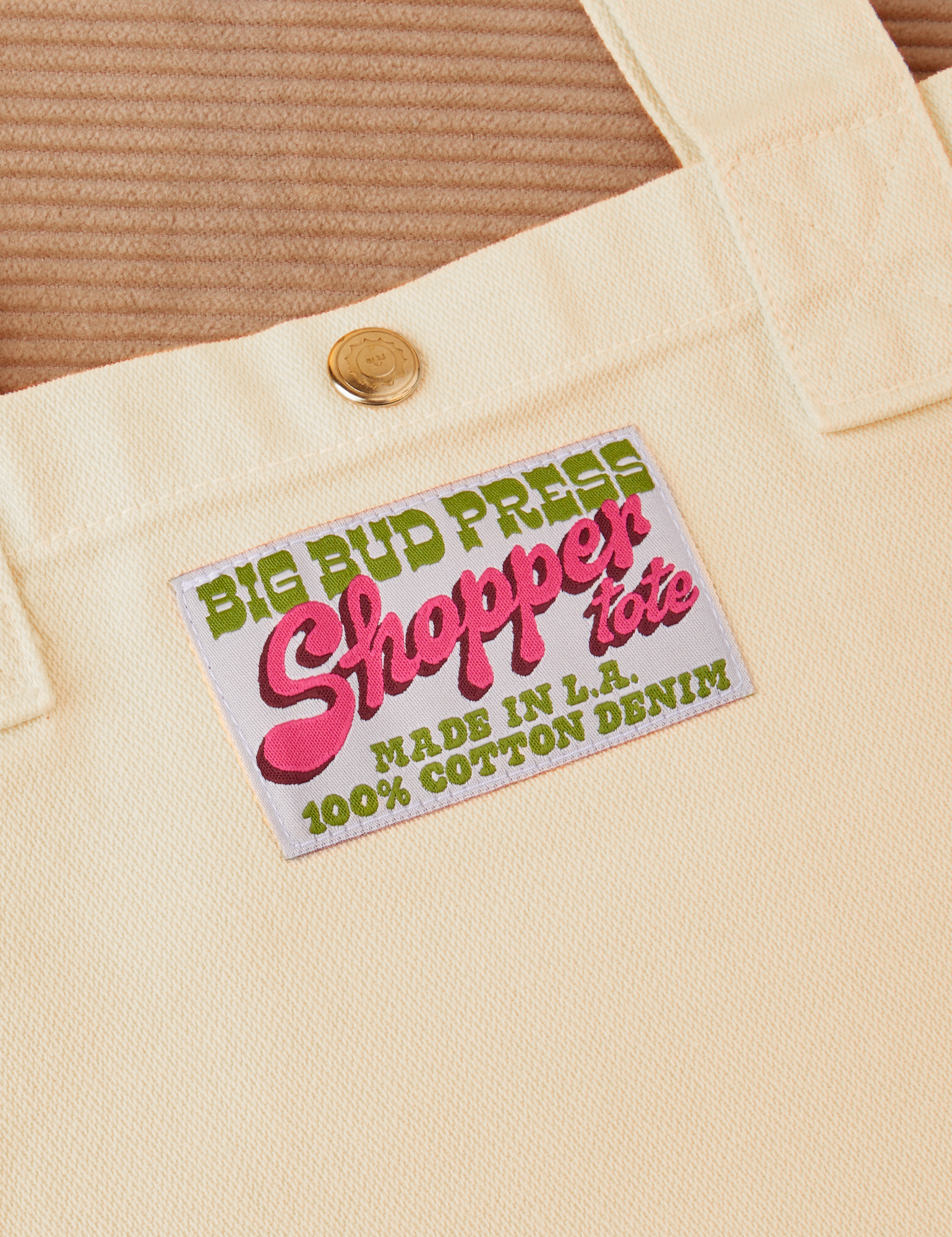 Sun Baby brass snap on Shopper Tote Bag in Vintage Off-White. Bag label with green and pink text that reads &quot;Big Bud Press Shopper Tote, Made in L.A., 100% Cotton Denim&quot; on a white background