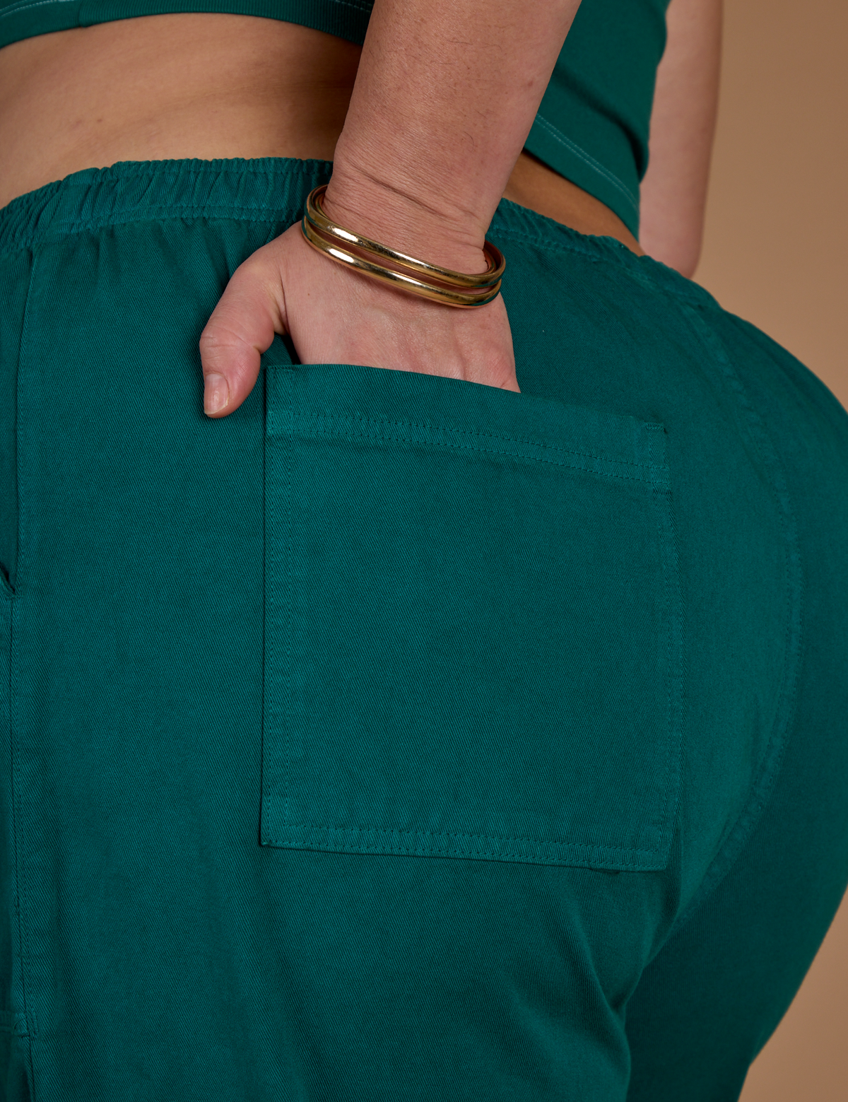 Close up of Kristen's hand in the back pocket of the Hunter Green Action Pant