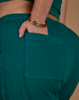 Close up of Kristen's hand in the back pocket of the Hunter Green Action Pant