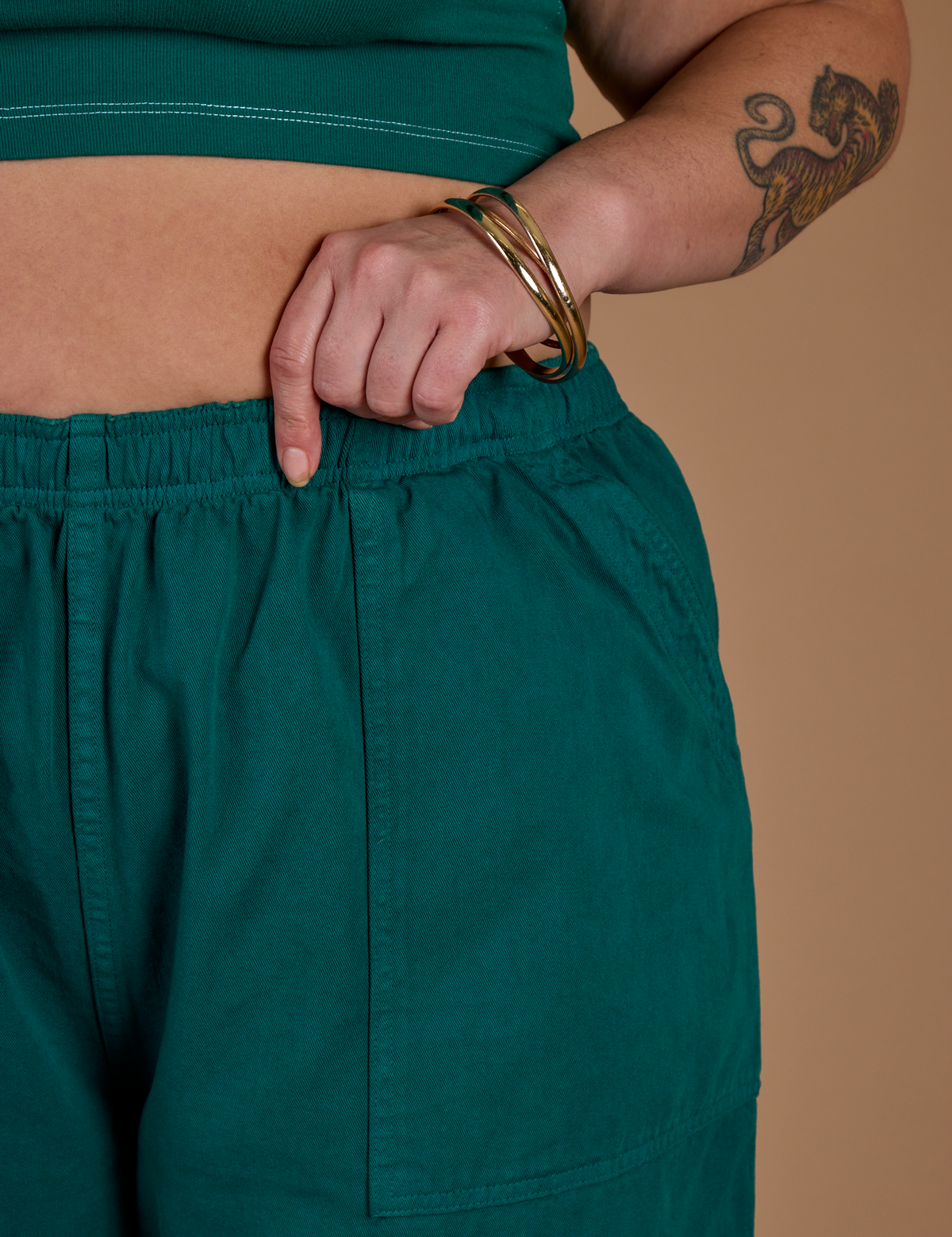 Close up of Kristen's hand on the waistband of the Hunter Green Action Pant