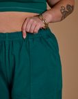 Close up of Kristen's hand on the waistband of the Hunter Green Action Pant