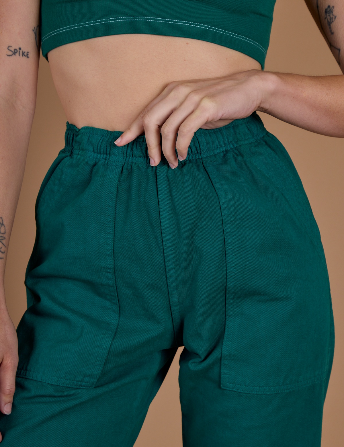 Close up of Alex's hand on the waistband of the Hunter Green Action Pant