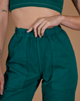 Close up of Alex's hand on the waistband of the Hunter Green Action Pant
