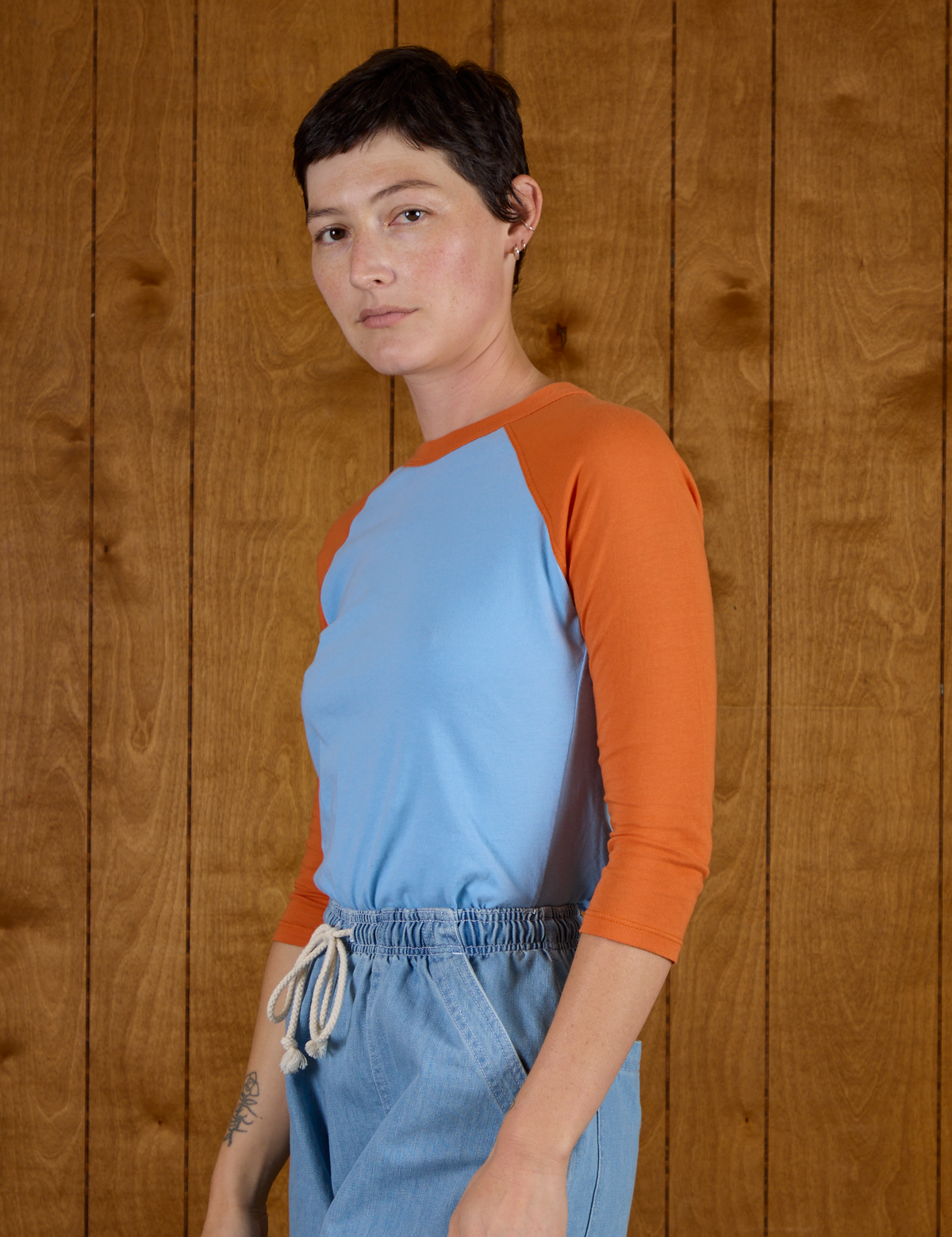 Angled side view of Alex wearing the Baby Blue/Orange Colorblock Raglan Tee