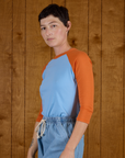 Angled side view of Alex wearing the Baby Blue/Orange Colorblock Raglan Tee