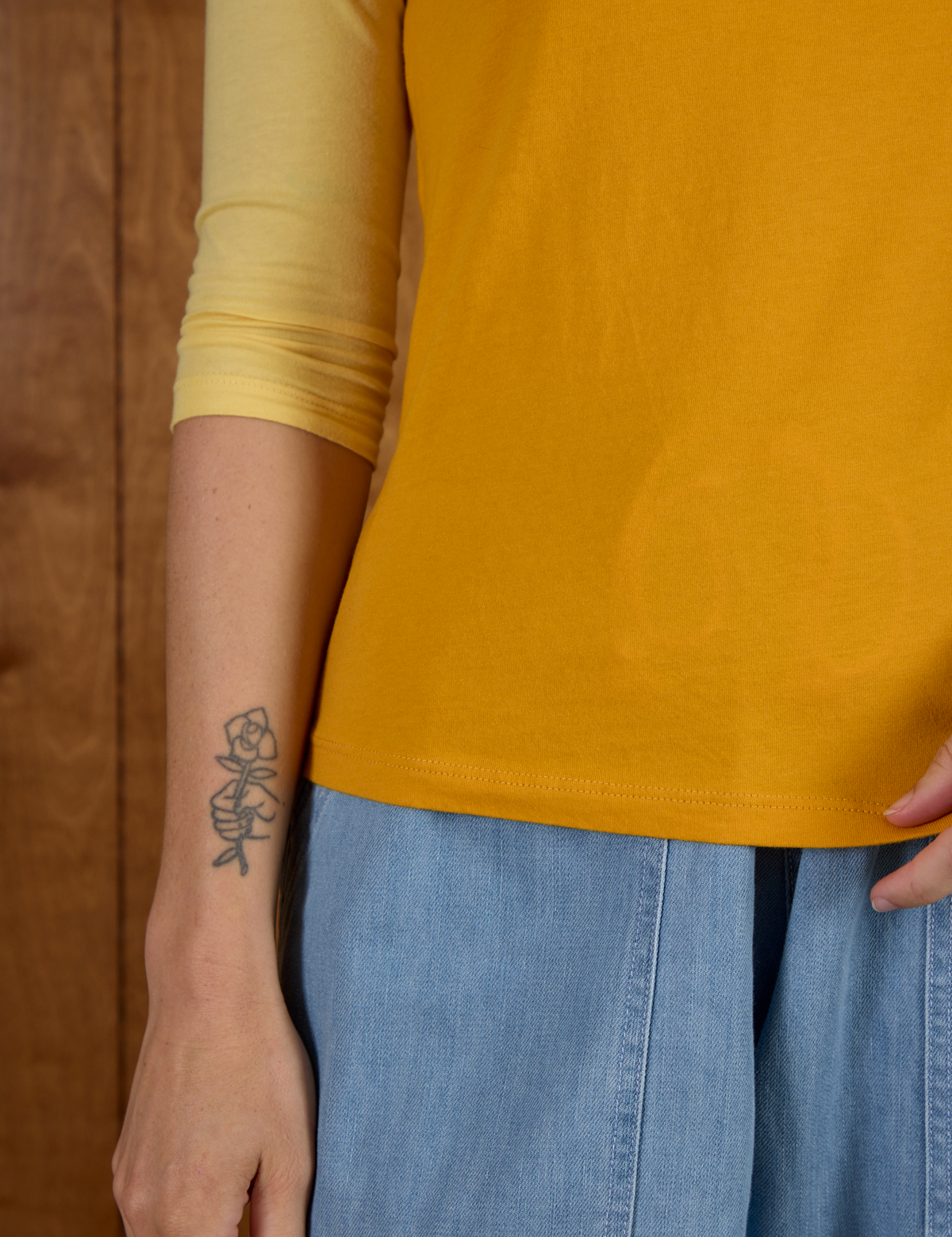 Close up of hemline on the Mustard Yellow/Butter Raglan Tee worn by Alex