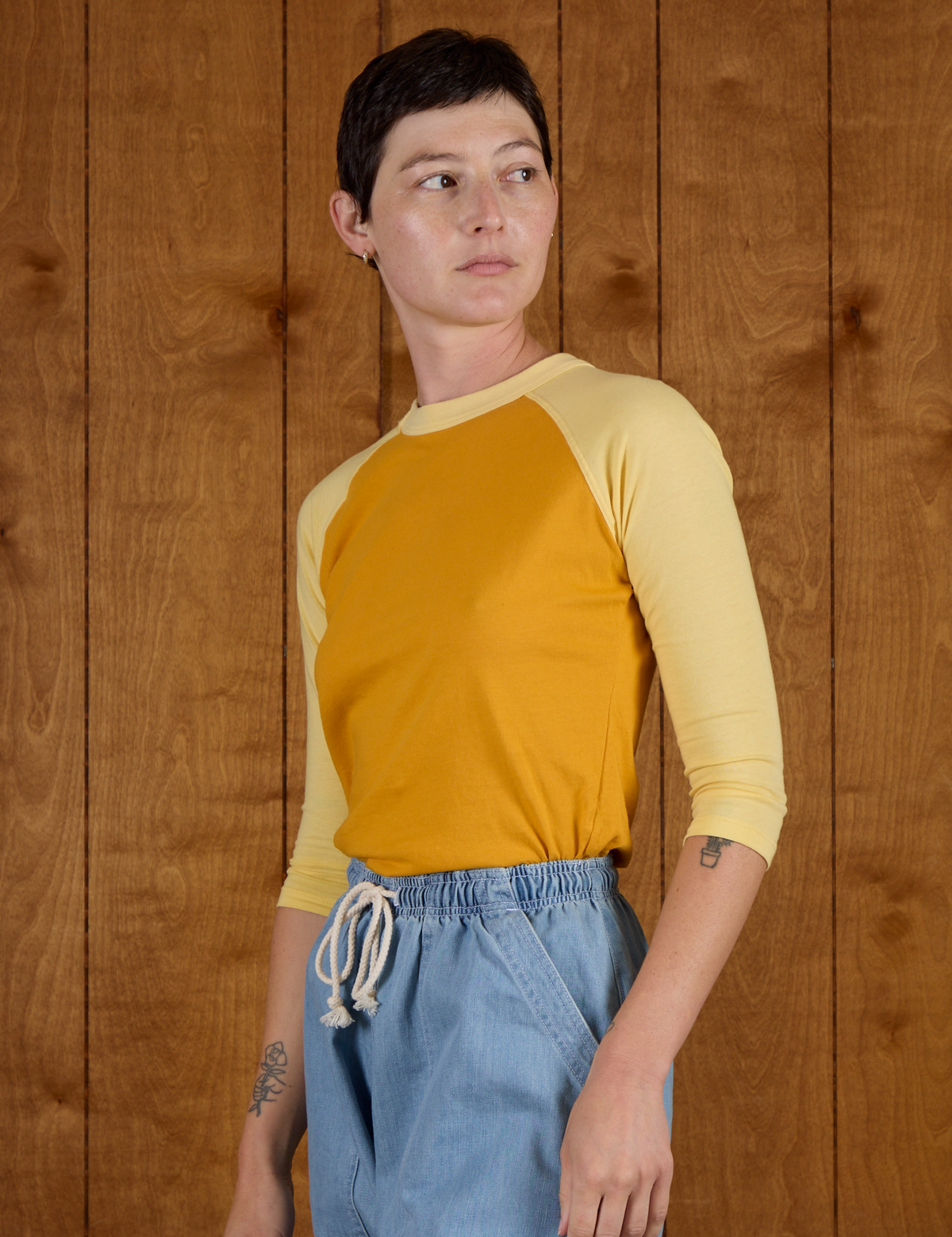 Angled side view of Alex wearing the Mustard Yellow/Butter Raglan Tee