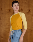 Angled side view of Alex wearing the Mustard Yellow/Butter Raglan Tee
