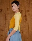 Angled back view of the Mustard Yellow/Butter Raglan Tee on Alex
