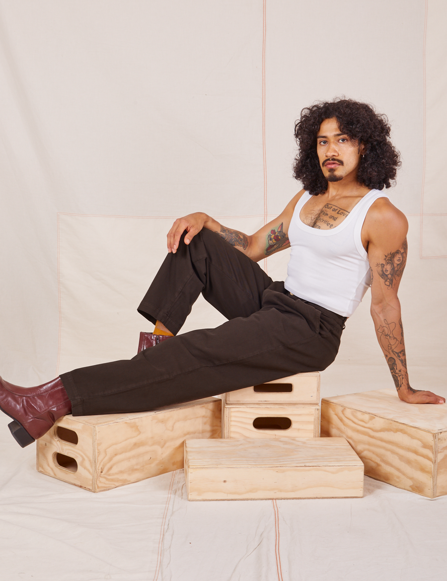 Jesse is sitting on a wooden crate. They are wearing Heavyweight Trousers in Espresso Brown and vintage off-white Cropped Tank Top.
