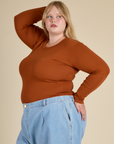 Angled side view of the Burnt Terracotta Long Sleeve Baby Tee on Juliet