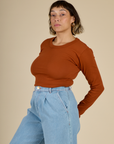 Angled side view of Tiara in the Burnt Terracotta Long Sleeve Baby Tee
