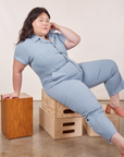 Ashley is wearing Petite Short Sleeve Jumpsuit in Periwinkle and sitting on a stack of wooden crates