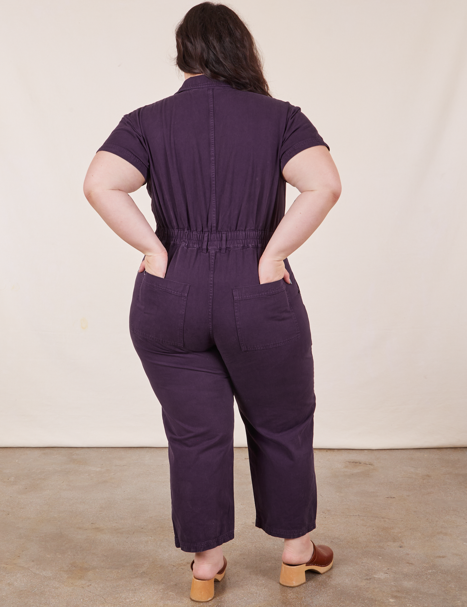 Back view of Petite Short Sleeve Jumpsuit in Nebula Purple. Ashley has both hands in the pocket.
