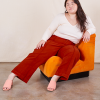 Ashley is sitting on an orange upholstered chair. She is wearing Western Pants in Paprika paired with a vintage off-white Long Sleeve V-Neck Tee