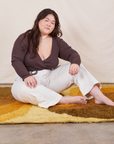 Ashley is sitting on a yellow rug wearing Western Pants in Vintage Off-White and an espresso brown Wrap Top