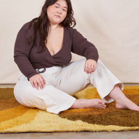 Ashley is sitting on a yellow rug wearing Western Pants in Vintage Off-White and an espresso brown Wrap Top