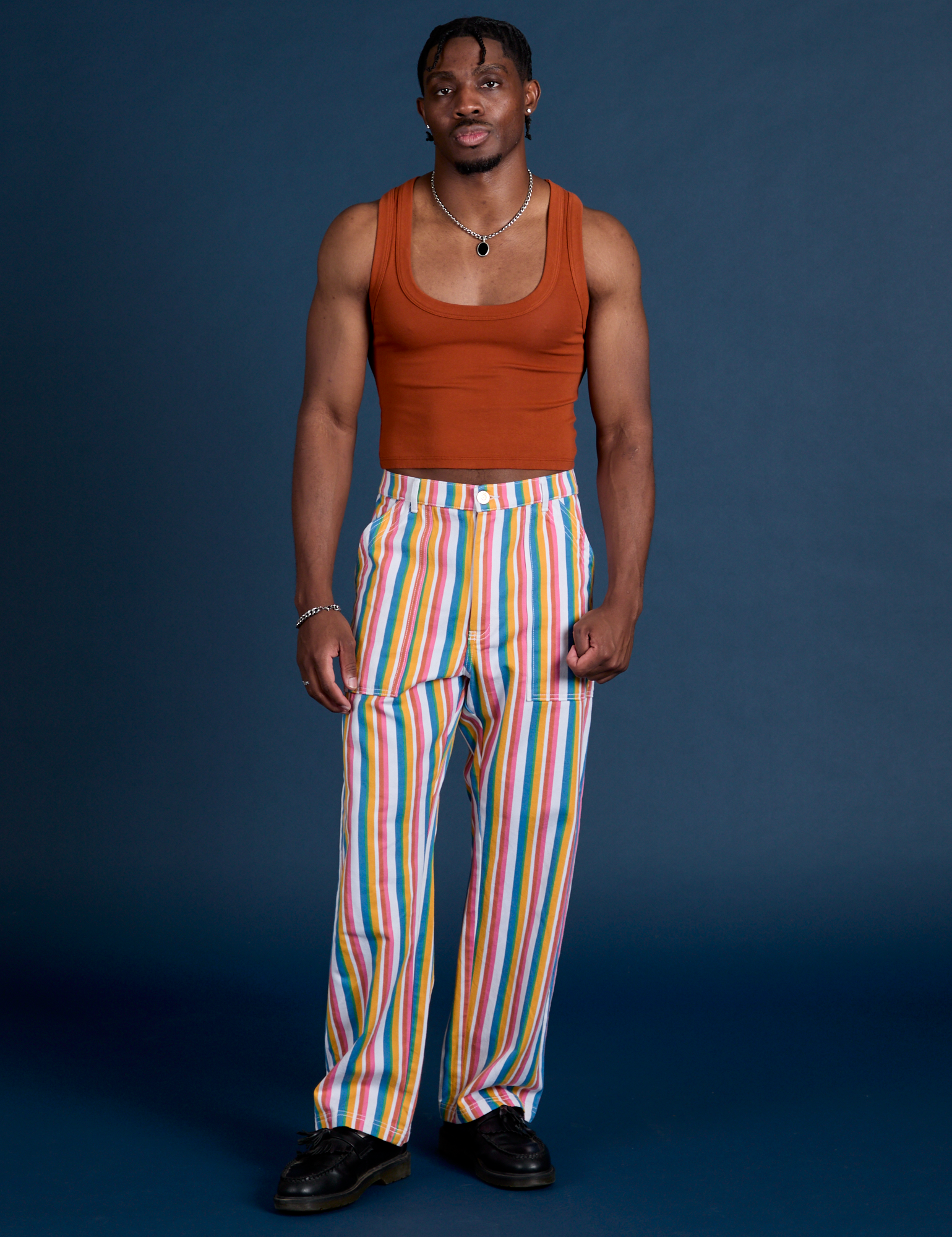 Isaac is wearing Work Pants in Rainbow Stripe and burnt terracotta Cropped Tank