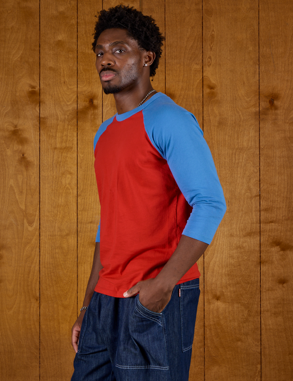Angled side view of Isaac wearing the Mustang Red/Blue Colorblock Raglan Tee