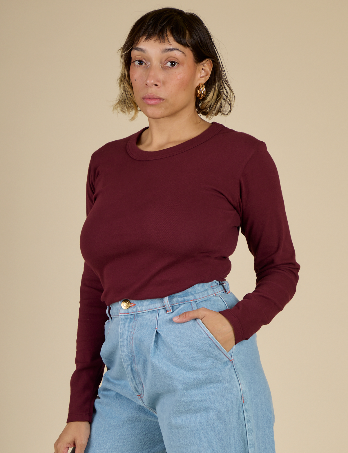 Angled side view of Tiara wearing the Red Wine Long Sleeve Baby Tee tucked in