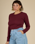 Angled side view of Tiara wearing the Red Wine Long Sleeve Baby Tee tucked in