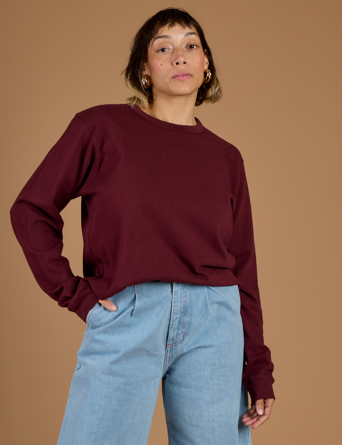 Tiara is wearing the Red Wine Long Sleeve Burly Tee tucked into the Light Wash Wide Leg denim Trousers