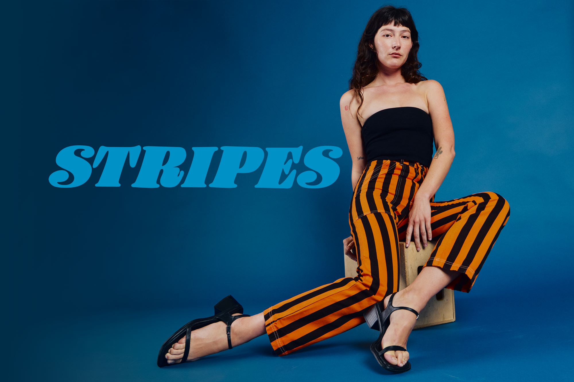 Alex is wearing black tube top paired with construction orange black stripe work pants