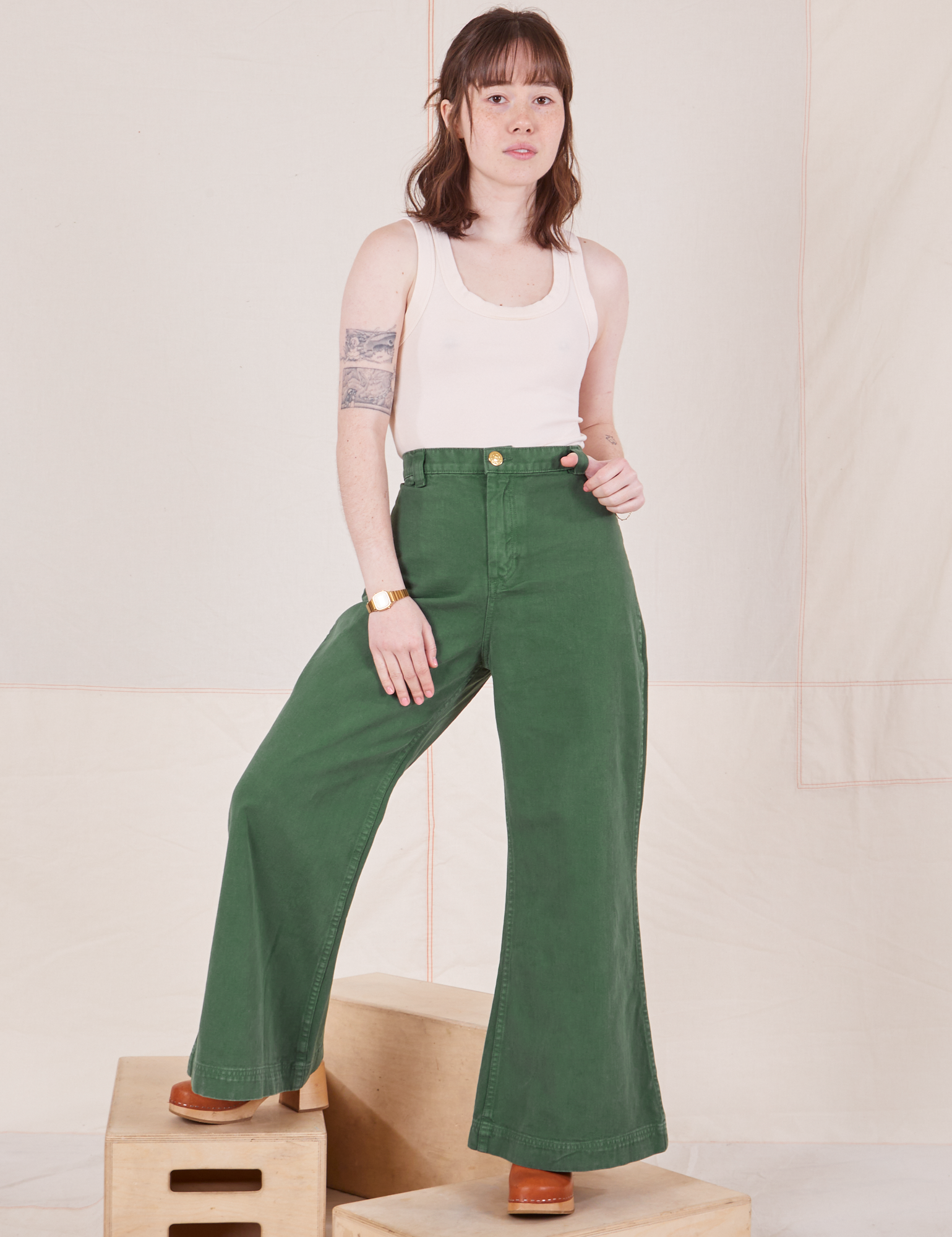 Hana is 5&#39;3&quot; and wearing XXS Bell Bottoms in Dark Emerald Green paired with vintage off-white Tank Top