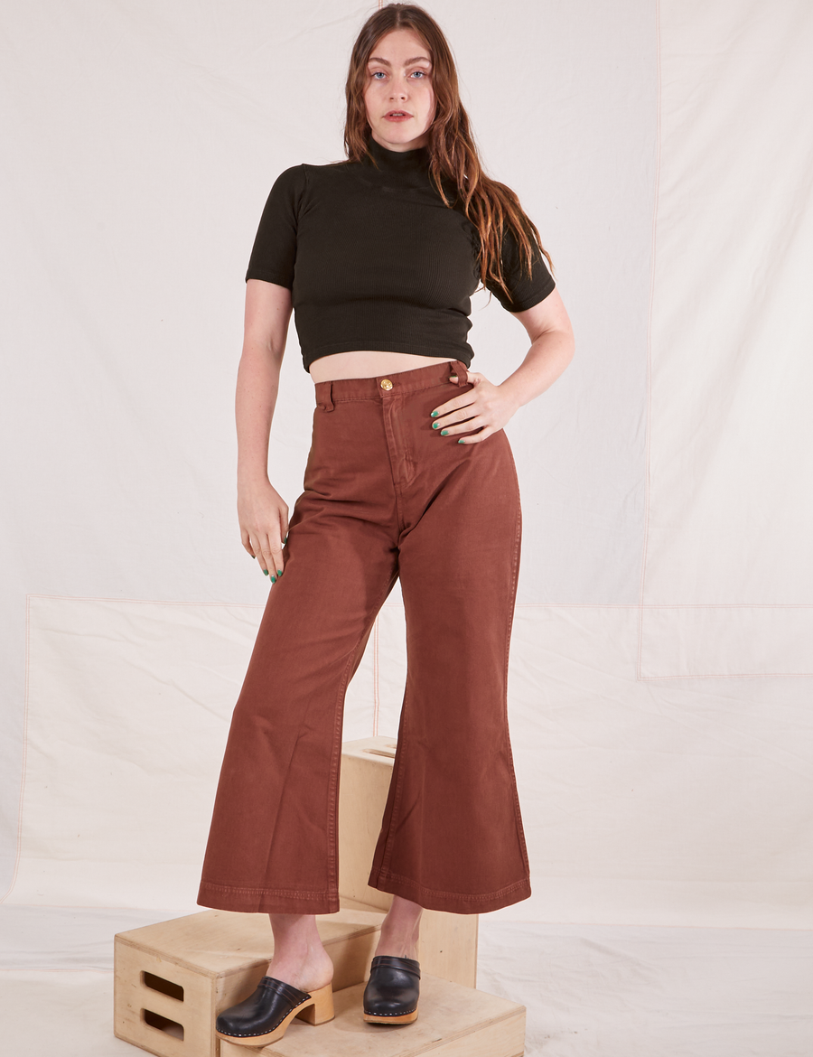 Allison is standing on a wooden crate wearing 1/2 Sleeve Essential Turtleneck in Espresso Brown and fudgesicle brown Bell Bottoms
