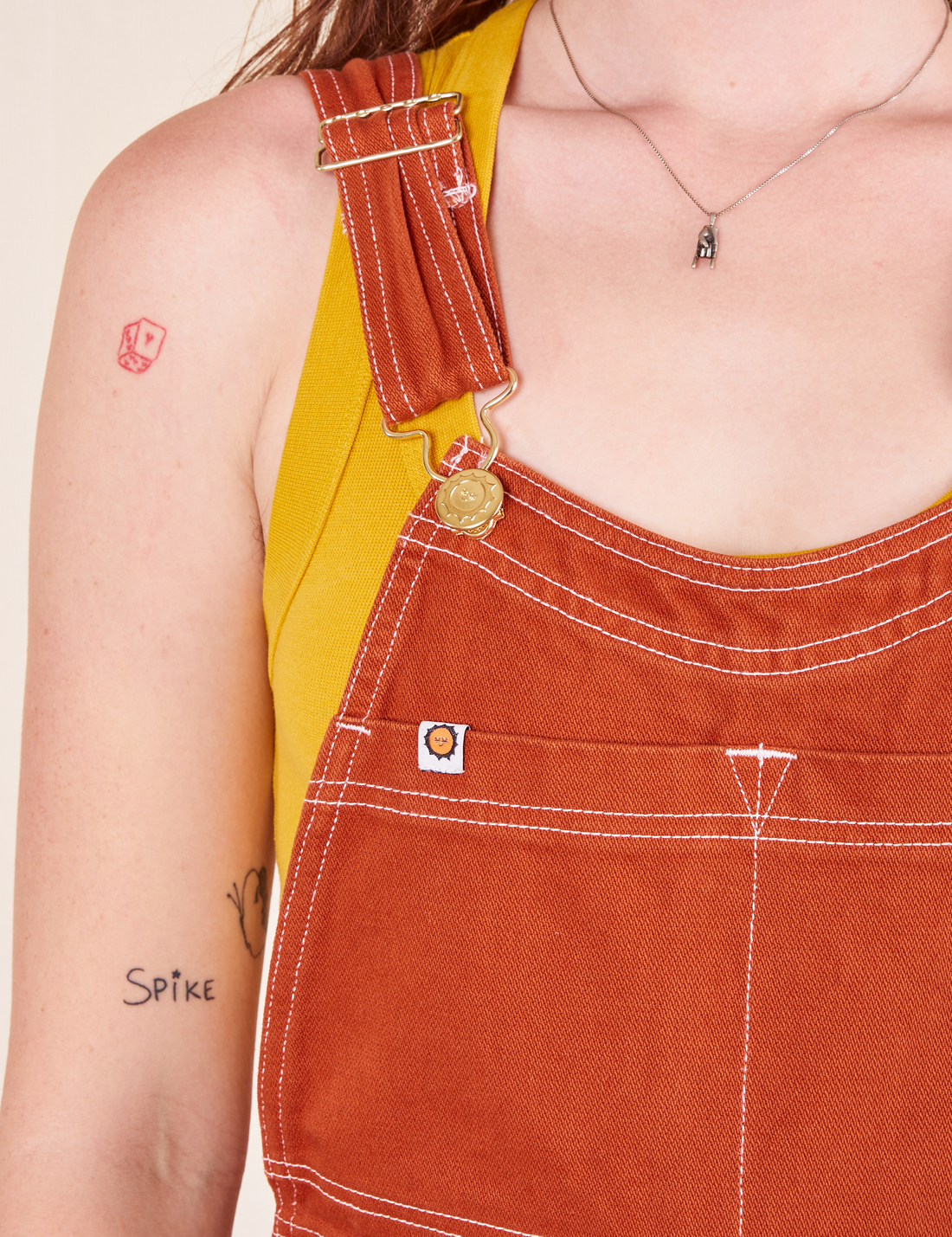 Original Overalls in Burnt Terracotta front close up white stitching and gold hardware 