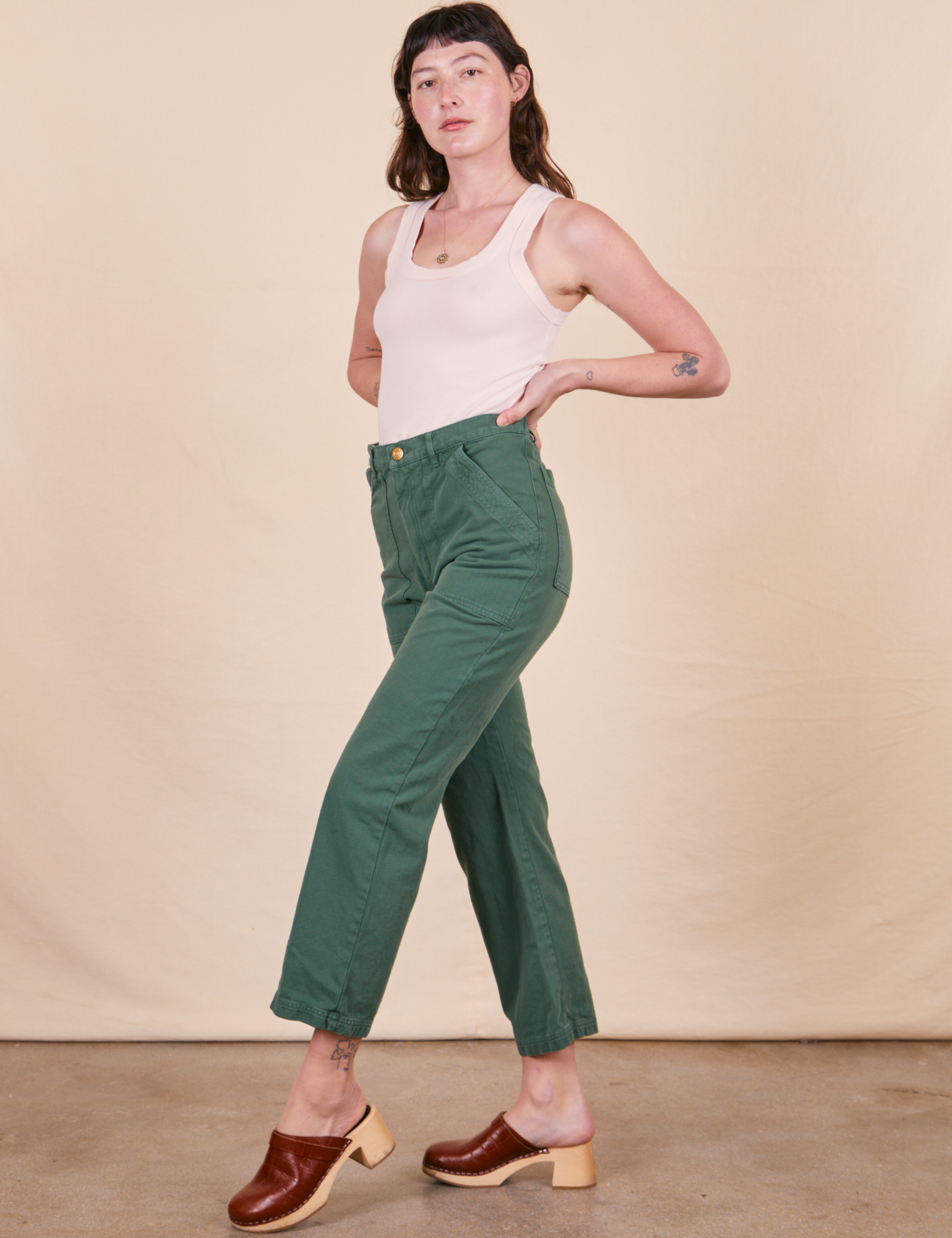Angled view of Work Pants in Dark Emerald Green and vintage off-white Tank Top
