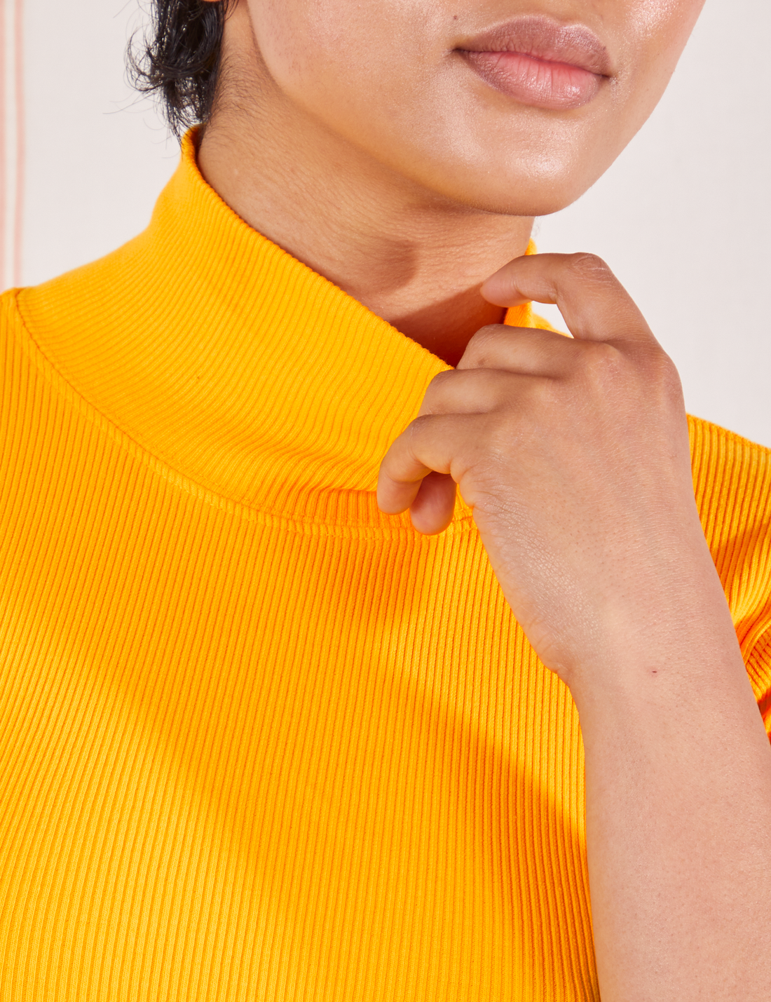 1/2 Sleeve Essential Turtleneck in Sunshine Yellow top front close up. Mika is holding onto the collar of the turtleneck