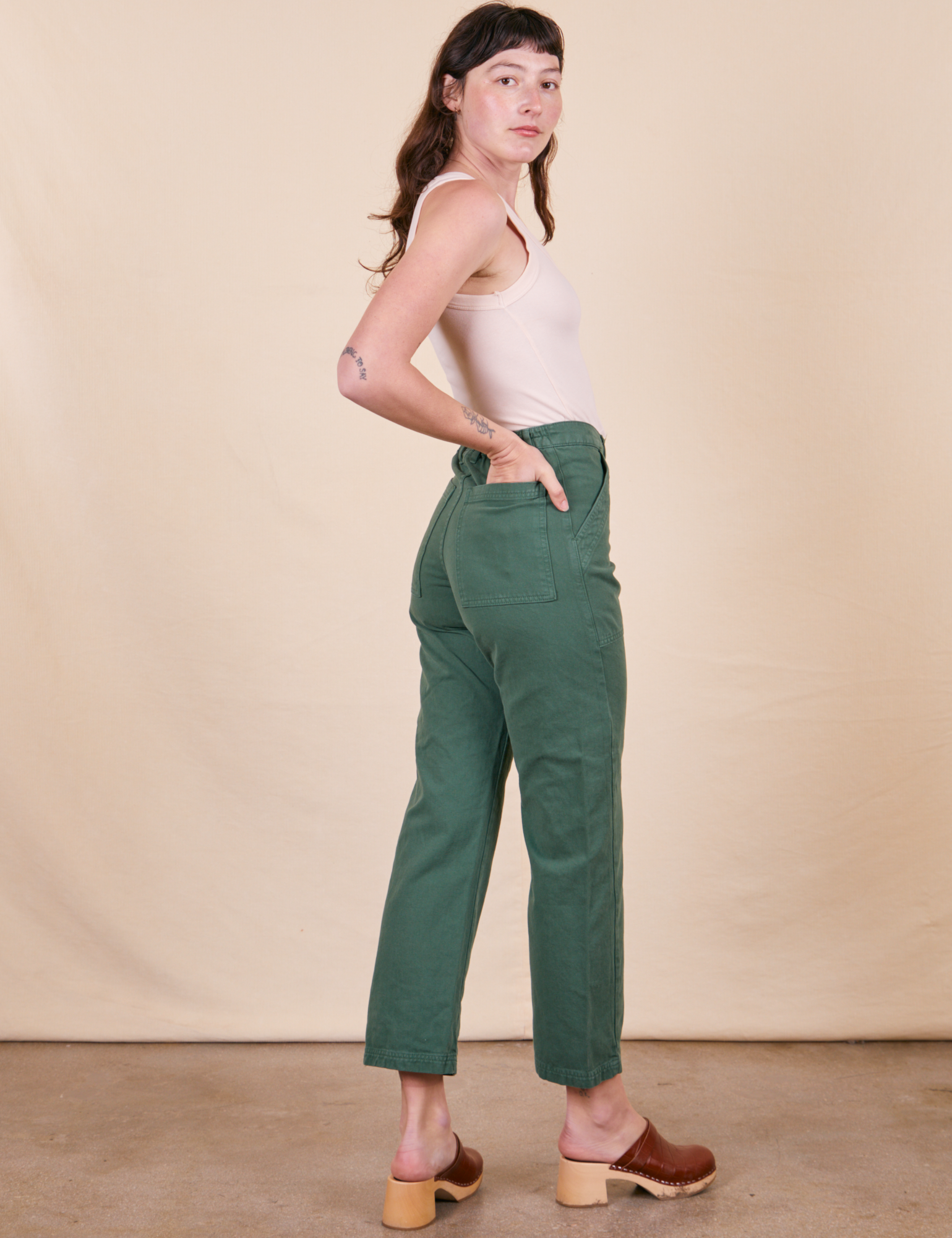 Back view of Work Pants in Dark Emerald Green and vintage off-white Tank Top worn by Alex