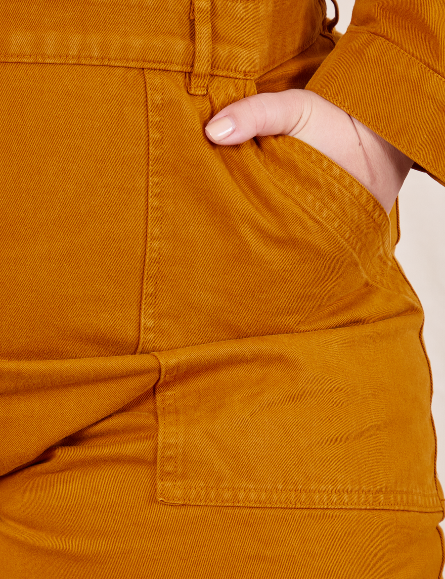 Front pocket close up of Everyday Jumpsuit in Spicy Mustard. Ashley has her hand in the pocket.
