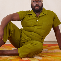 Elijah is sitting on a rug wearing Short Sleeve Jumpsuit in Olive Green