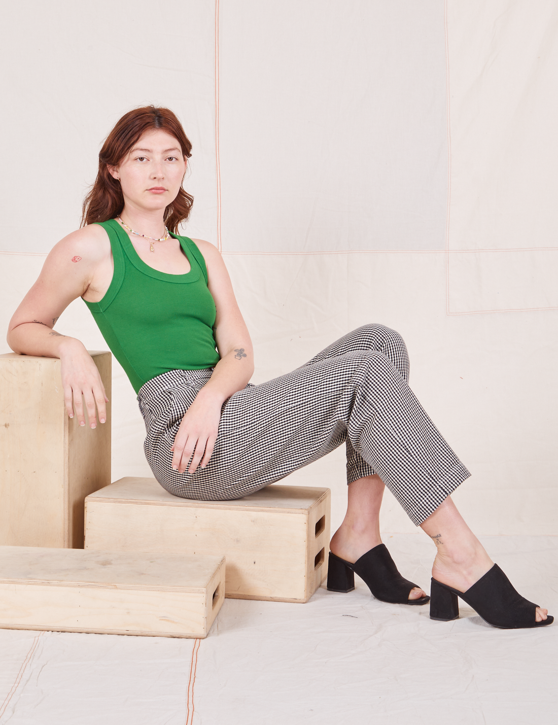 Alex is sitting on a wooden crate wearing Checker Trousers in Black & White and forest green Tank Top