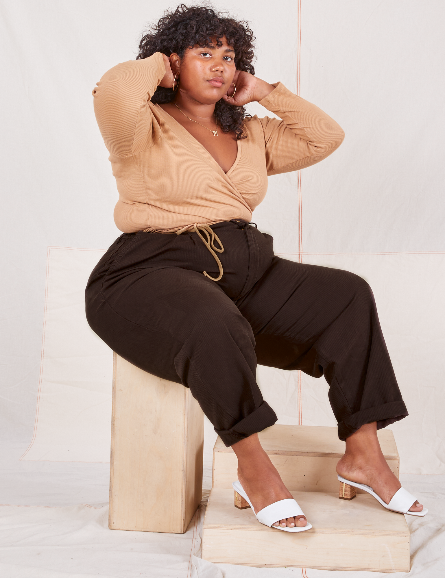 Heritage Trousers in Espresso Brown on Morgan sitting on wooden crate wearing tan Wrap Top