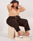 Heritage Trousers in Espresso Brown on Morgan sitting on wooden crate wearing tan Wrap Top
