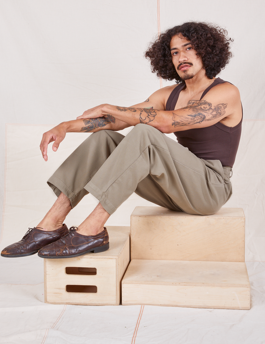 Jesse is wearing Heritage Trousers in Khaki Grey and espresso brown Tank Top