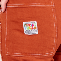 Back pocket close up of Original Overalls in Burnt Terracotta. Alex has her hand in the pocket.
