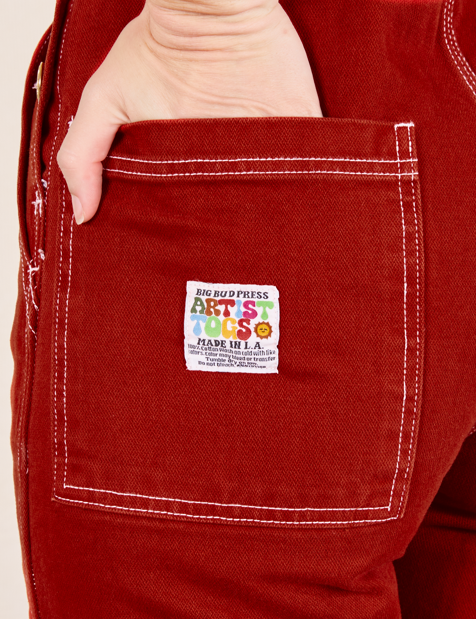Back pocket close up of Original Overalls in Paprika. Alex has her hand in the pocket.