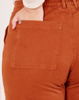 Back pocket close up of Organic Work Pants in Burnt Terracotta. Melanie has her hand in the pocket.